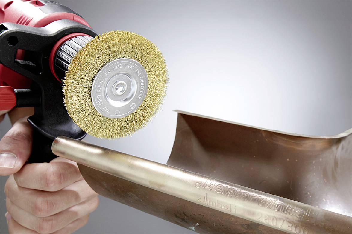 Eine Person nutzt eine Drahtbürste an einem Werkzeug, um eine glänzende Metalloberfläche zu polieren.