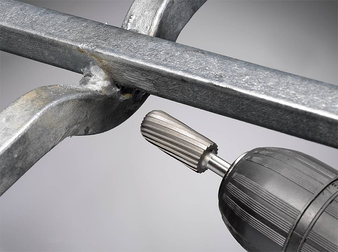 Bohrmaschine bearbeitet Metall, zeigt Nahaufnahme eines rotierenden Schleifaufsatzes an einem Stahlträger, Funken sprühen leicht.