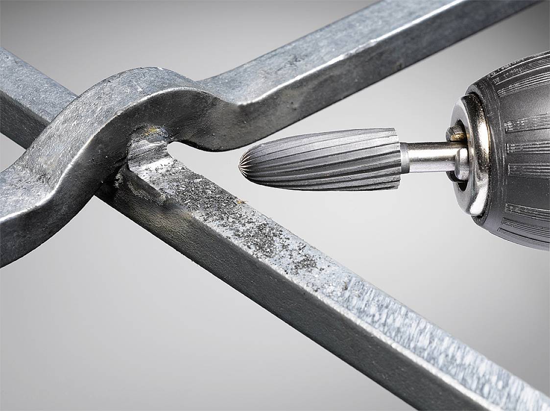 Ein Bohrer schleift Metallstäbe. Nahaufnahme zeigt Details des Werkzeugs und der bearbeiteten Oberfläche.