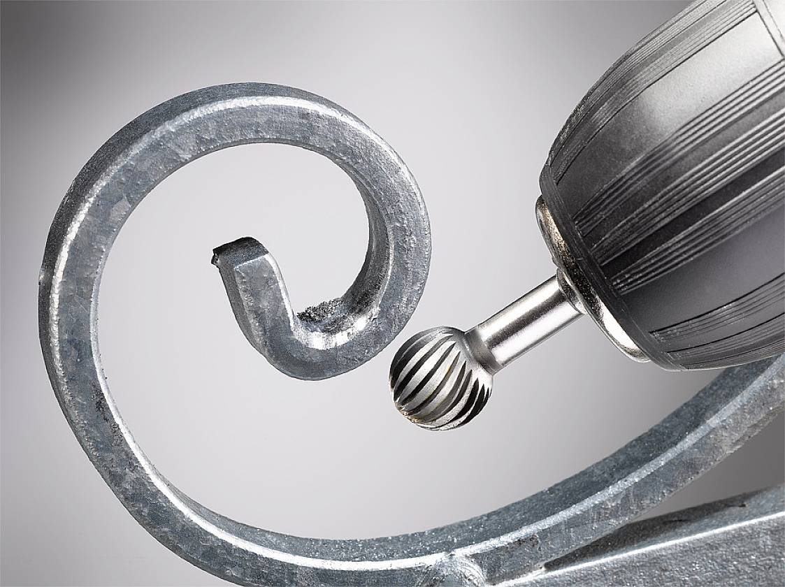 Eine elektrische Bohrmaschine mit einem Kugelfräser bearbeitet kunstvoll geschwungenes Metall, Nahaufnahme.