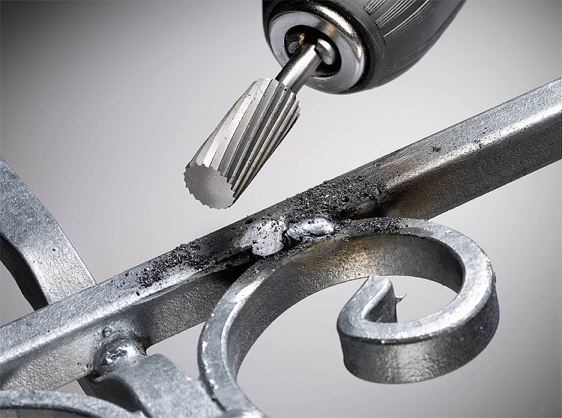 Ein Dremel-Werkzeug bearbeitet eine metallische Oberfläche, entfernt Rost und glättet die Kanten eines dekorativen Metallgitters.