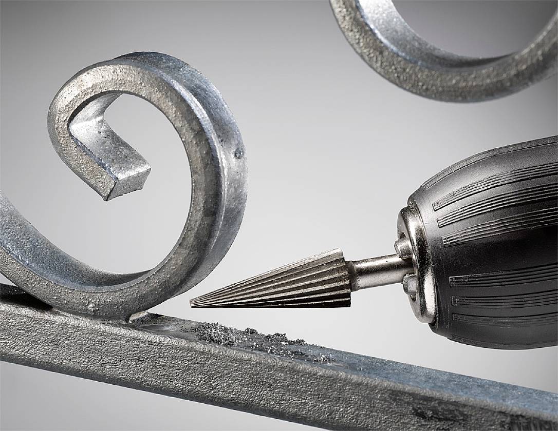 Bohrer mit Kegelfräser bearbeitet Metallstück mit einer Spiraldekoration, Metallspäne sichtbar. Nahaufnahme, zeigt präzises Arbeiten.