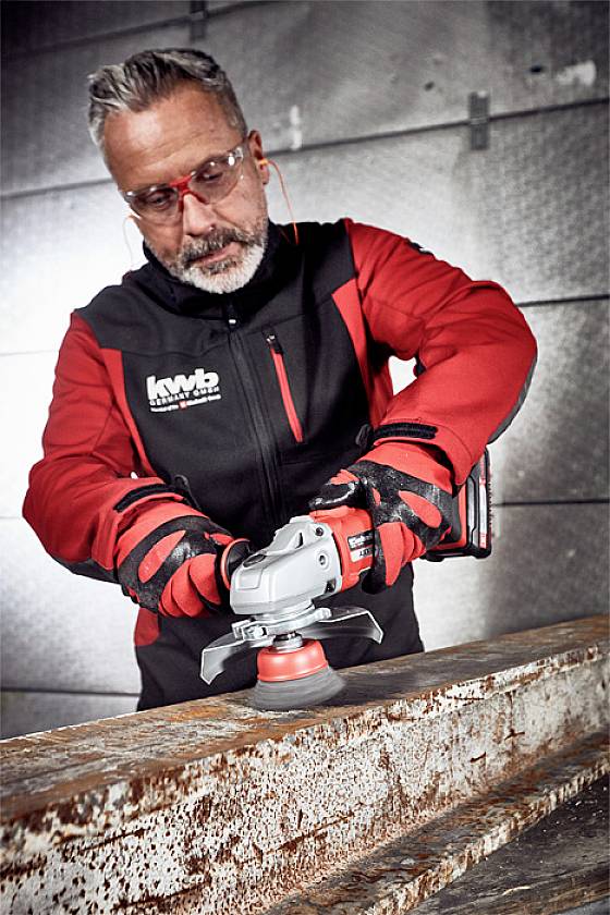 Ein Mann verwendet eine elektrische Schleifmaschine, um Rost von einer Metalloberfläche zu entfernen. Er trägt Schutzkleidung und -brille.