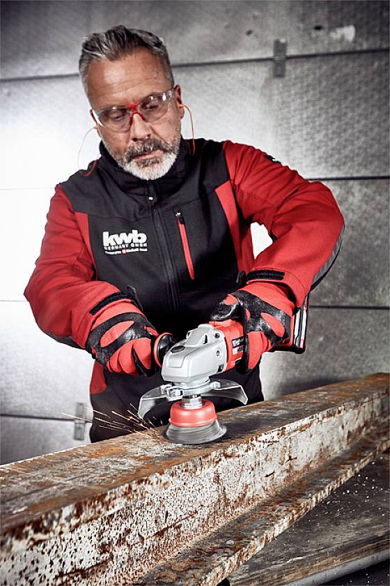 Eine Person in Arbeitskleidung schleift mit einem Winkelschleifer rostiges Metall. Funken sprühen, Schutzbrille und Handschuhe werden getragen.