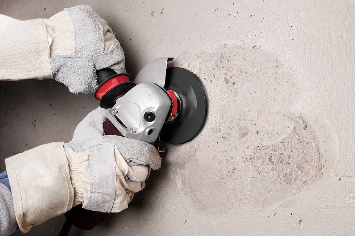 Eine Person trägt Handschuhe und verwendet eine Schleifmaschine, um eine Betonoberfläche zu glätten.