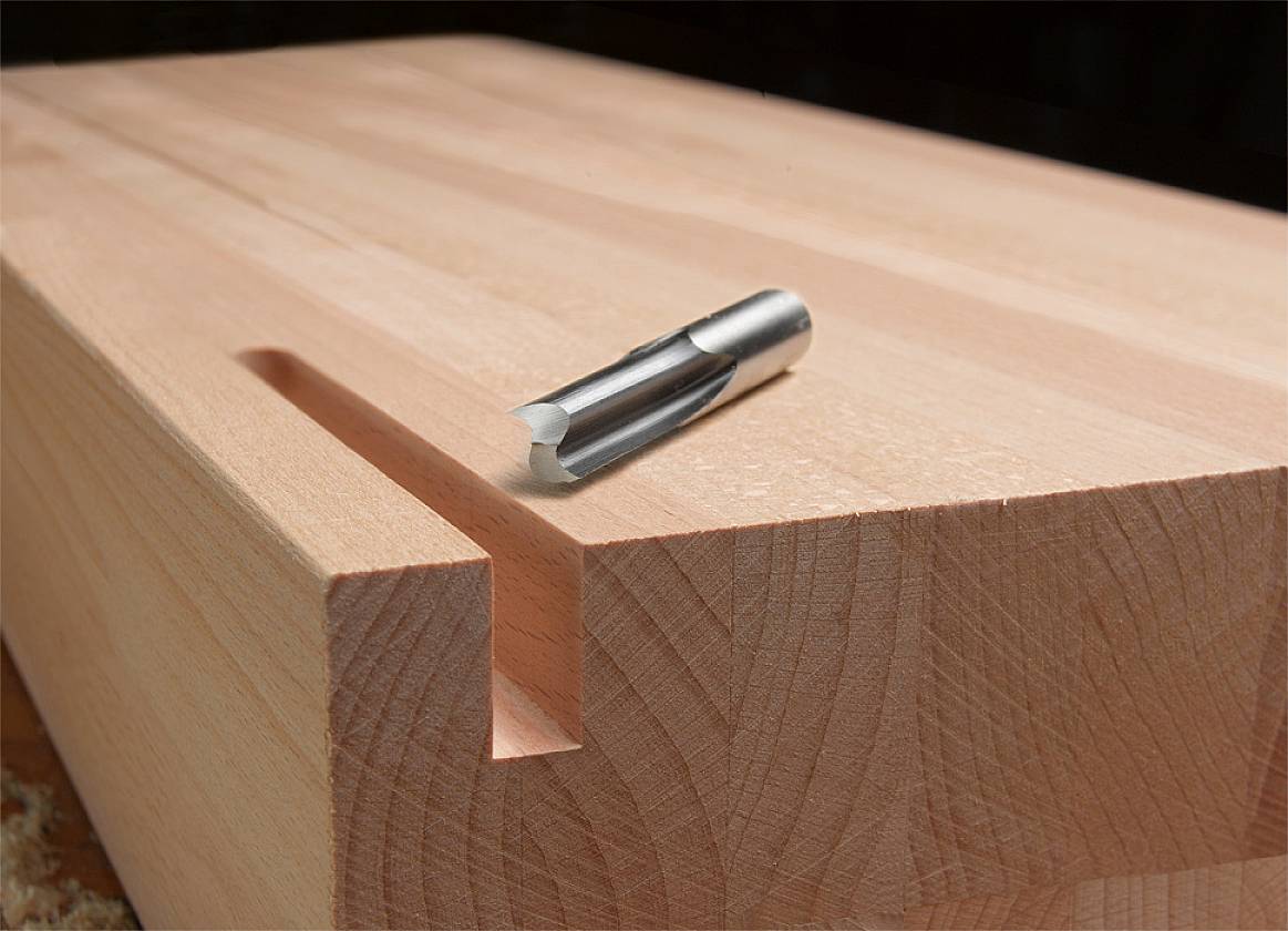 Holzstück mit gefräster Nut. Ein Fräser liegt auf der Oberfläche und zeigt Holzverarbeitung oder Tischlerei.