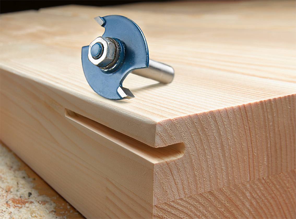 Oberfräse mit Rundfräser liegt auf einem Holzbrett neben frisch gefräster Nut; zeigt Holzverarbeitungstechnik.