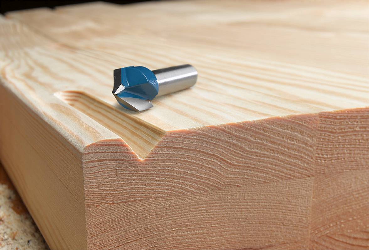 Ein Fräskopf liegt auf einem massiven Stück Holz mit einer gefrästen Kante, die die detailreiche Verarbeitung und Maserung zeigt.