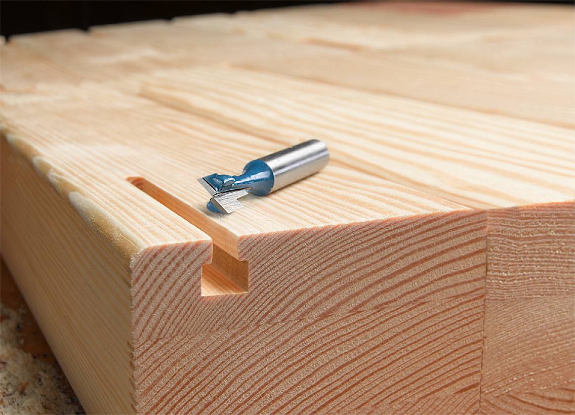 Eine gefräste Holzkante, auf der ein Fräser liegt. Der Fräser hat eine blaue Spitze. Das Holz zeigt eine Schwalbenschwanzverbindung.