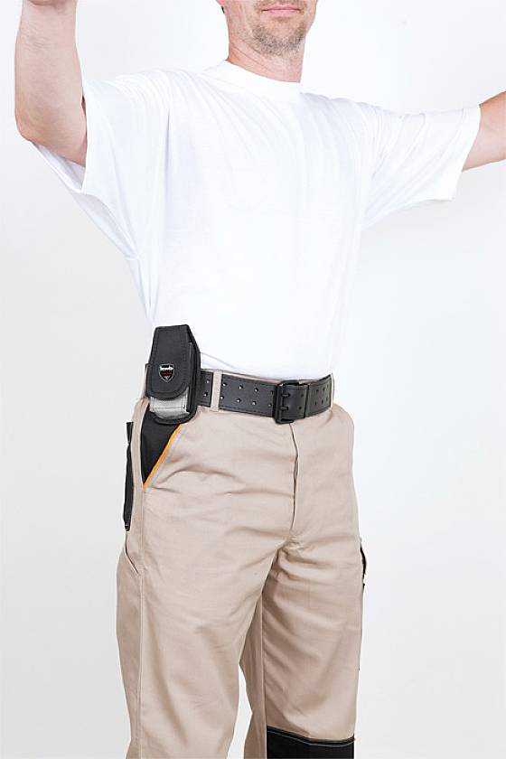 Mann trägt ein weißes T-Shirt und beige Hosen mit Schwarz. Er hat ein Holster am Gürtel. Gesicht nicht sichtbar.