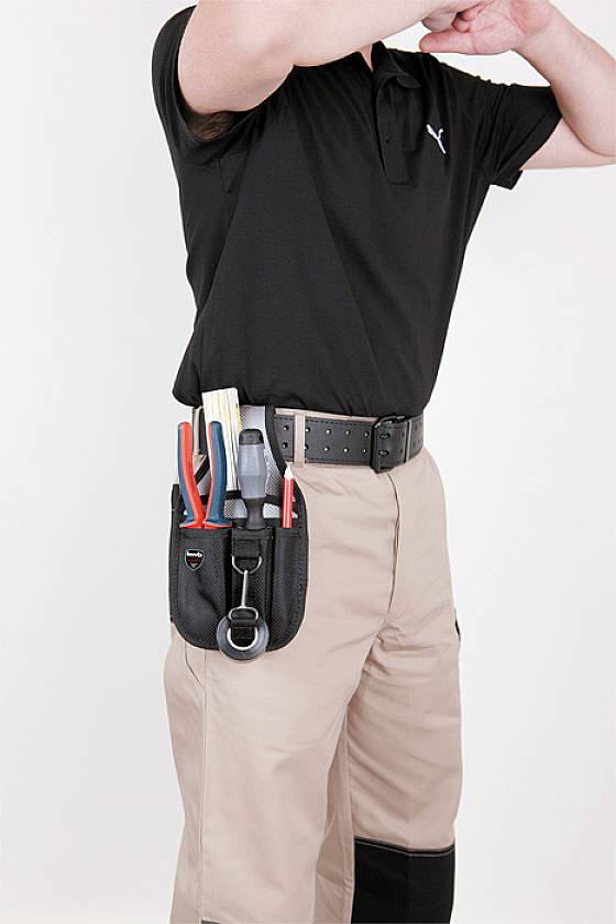 Person in schwarzem Polohemd und beige Hose mit Werkzeugtasche voller Werkzeuge an der Hüfte.