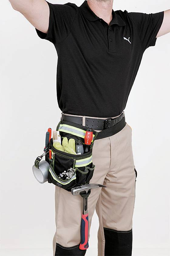 Nahaufnahme eines Handwerkers in beige Hose und schwarzem Polohemd, mit einem Werkzeuggürtel voller Werkzeuge wie Hammer und Zange.