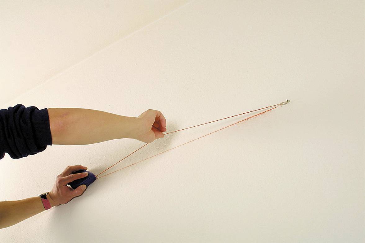 Eine Person zieht einen roten Faden mit einem Gerät an der Wand entlang, möglicherweise um eine Linie zu markieren.