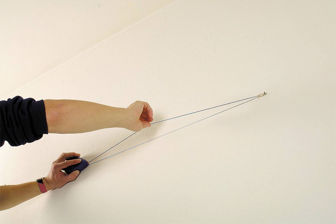 Eine Person demonstriert, wie man mit einem Gerät eine gerade Hilfslinie an einer Wand zieht, vermutlich um Bilder aufzuhängen.