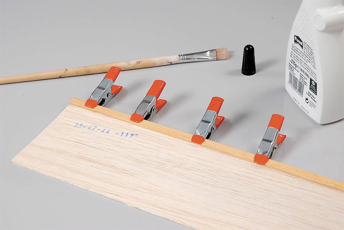 Holzbrett mit Klammern fixiert, umklebt und mit Leim, Pinsel und Deckel auf grauem Hintergrund vorbereitet. Werkzeuge für Holzbearbeitung.