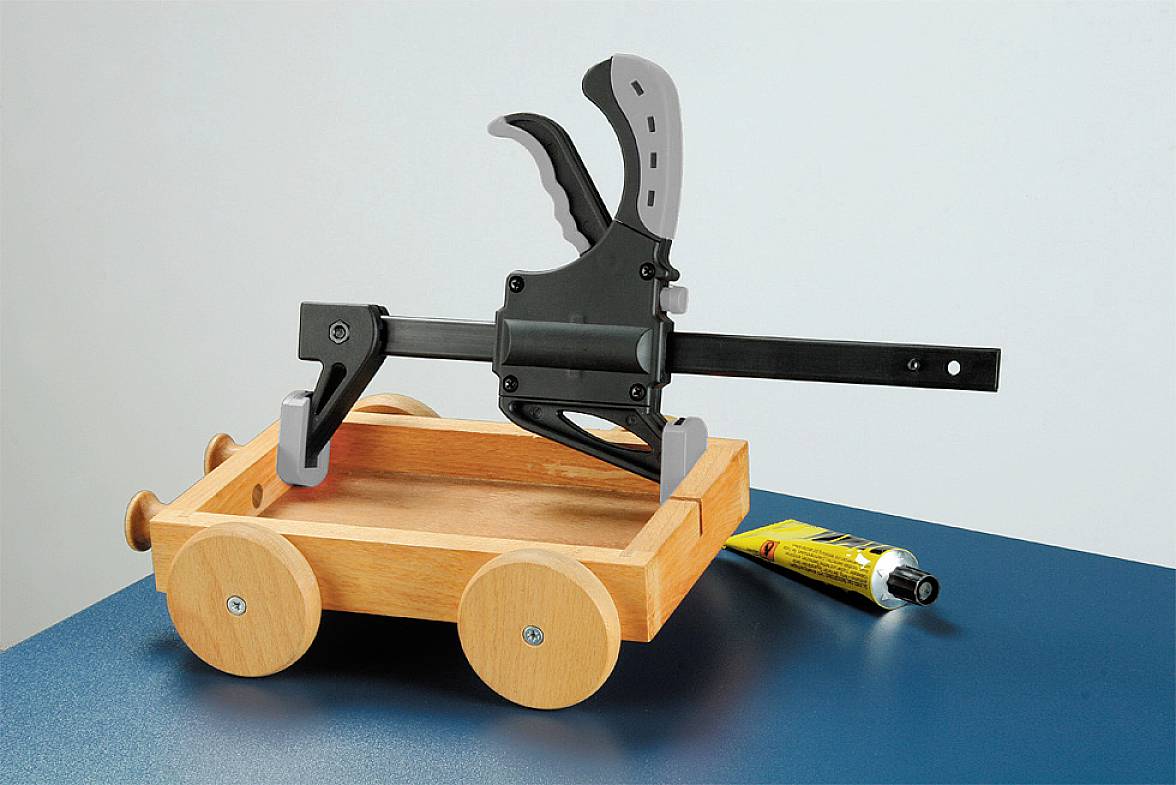 Holzwagen auf Tisch mit einem Schraubzwinge darauf; daneben liegt eine gelbe Klebertube.