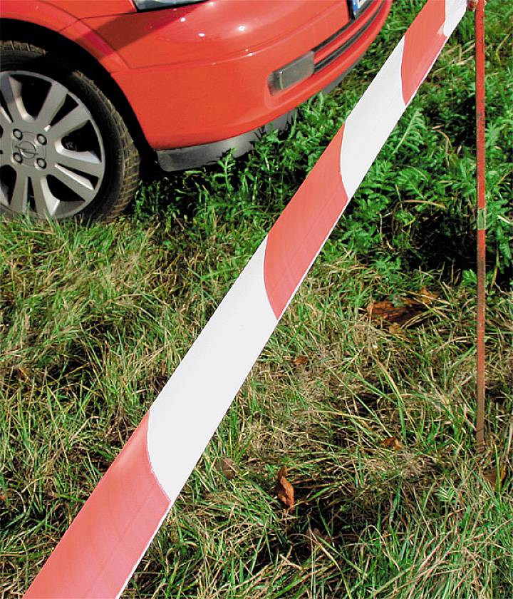 Rotes Auto geparkt neben einer rot-weißen Absperrung auf einer Wiese.