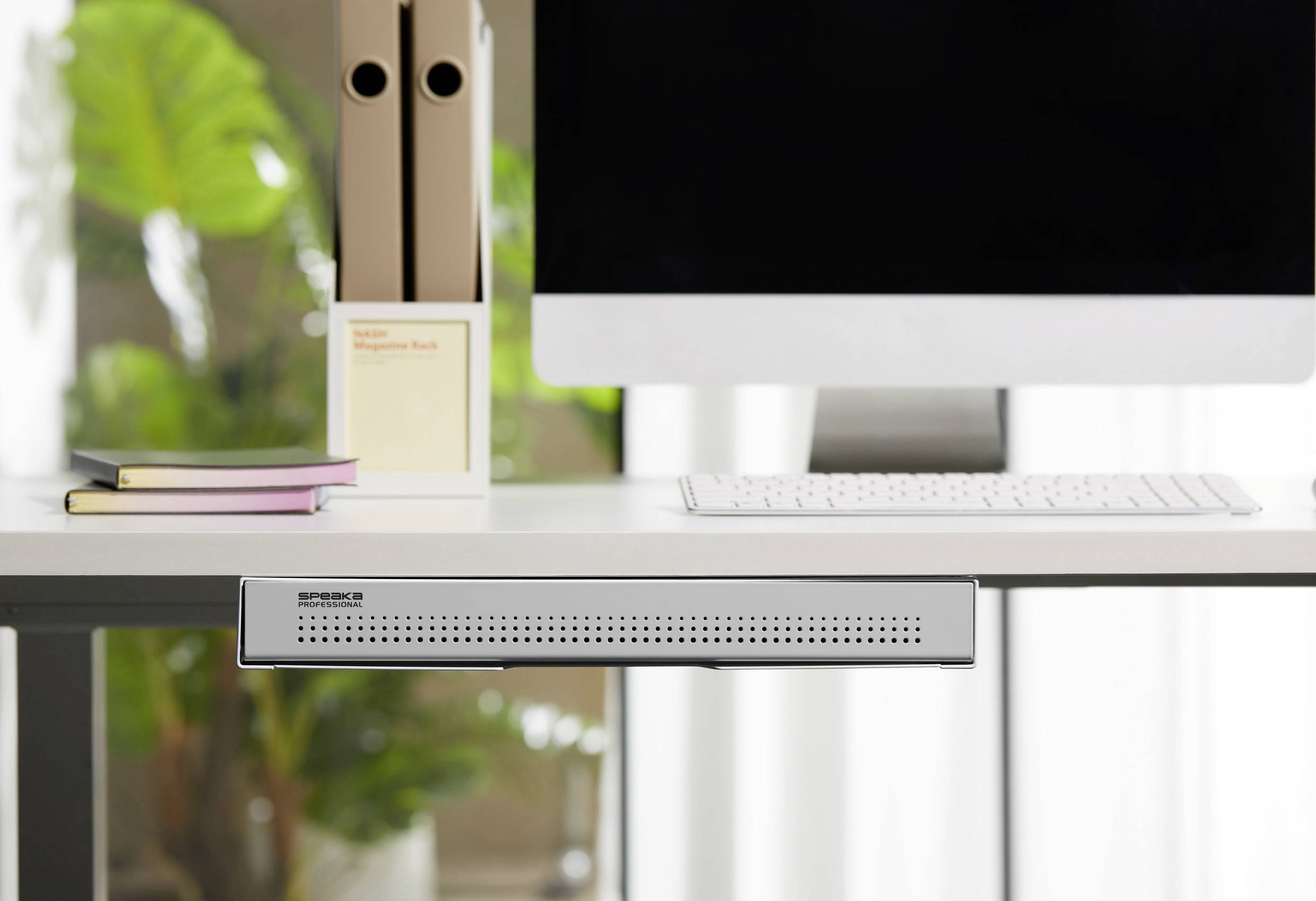 Ein moderner Schreibtisch mit einem Computerbildschirm, Tastatur, Aktenordnern und Pflanzen im Hintergrund.