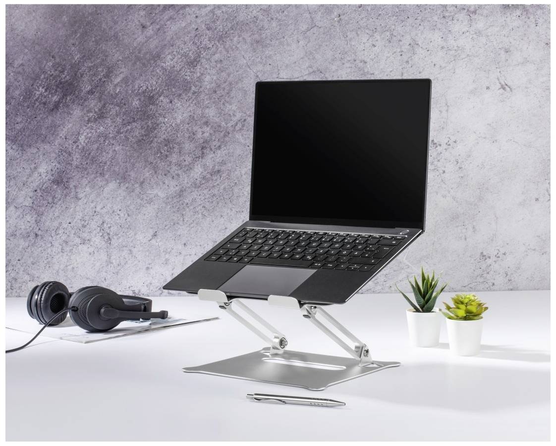 Ein Laptop steht auf einem höhenverstellbaren Ständer auf einem Schreibtisch, neben Kopfhörern und einer kleinen Pflanze.