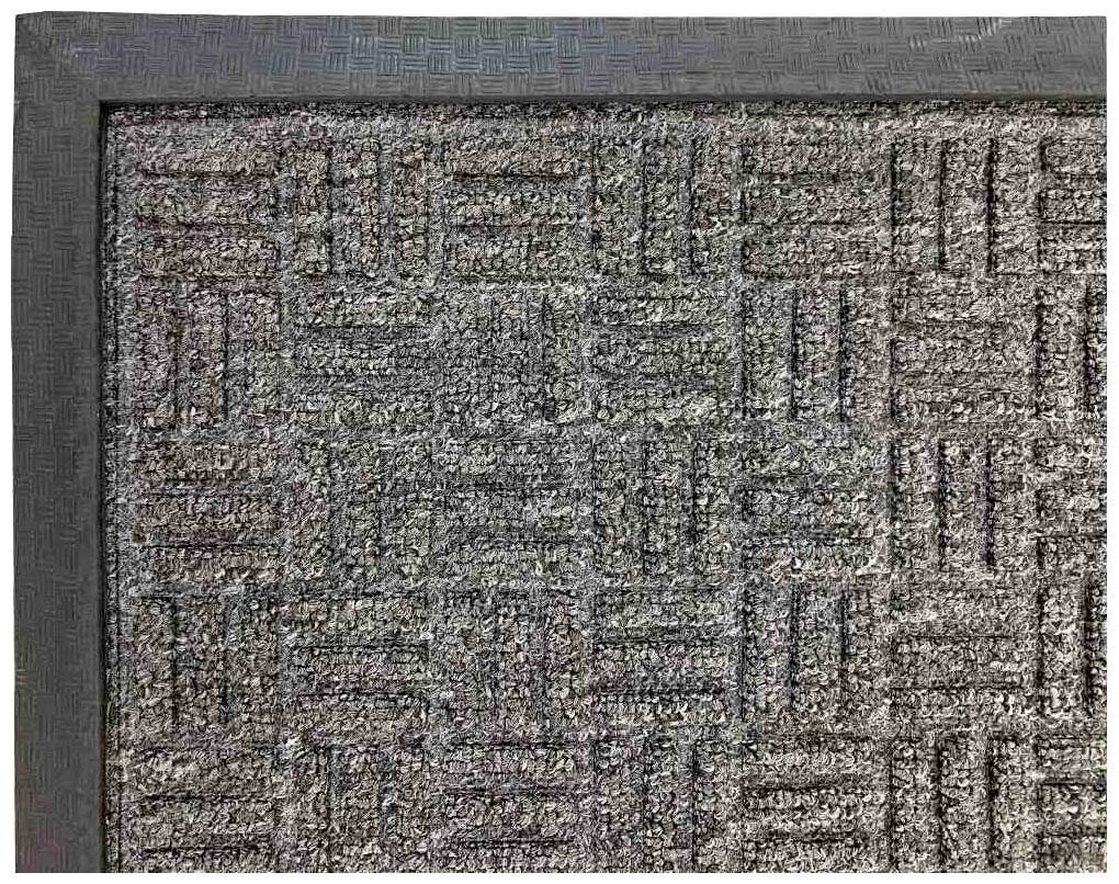 Eine graue Fußmatte mit geometrischem Muster liegt auf dem Boden und hat eine strukturierte Oberfläche und einen schwarzen Rand.