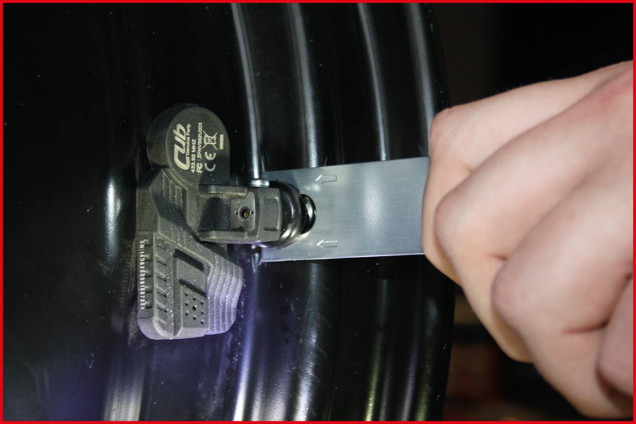 Nahaufnahme von einer Hand, die ein metallisches Band um einen schwarzen Zylinder spannt. Ein Sensor ist am Band befestigt.