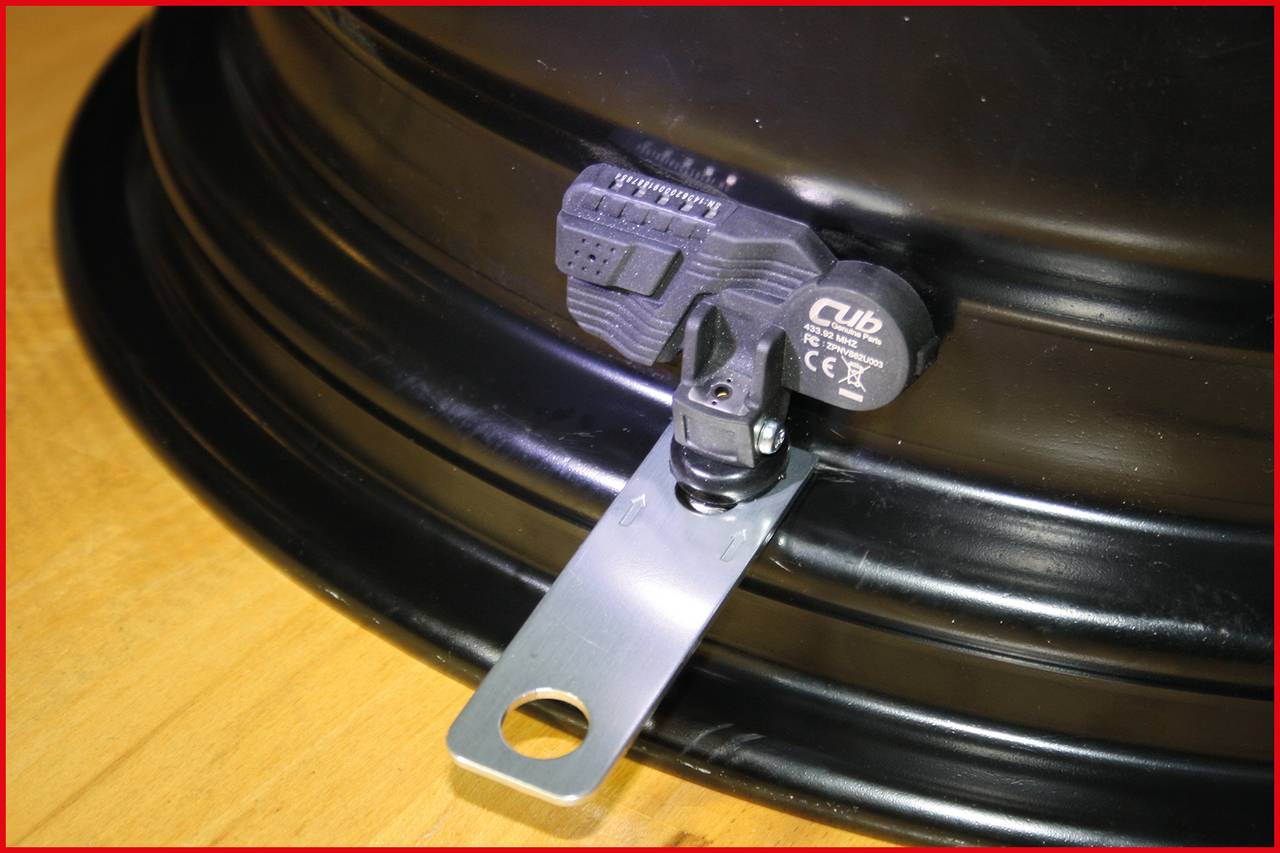 Ein Reifendrucksensor ist an einem Fahrzeugrad montiert, er zeigt Details der Halterung und des Sensors auf einer Metallfelge.