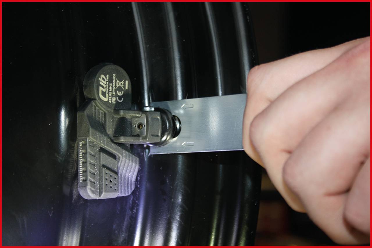 Ein Metallband wird um ein schwarzes Gerät gelegt, das an einer Reifenfelge angebracht ist.