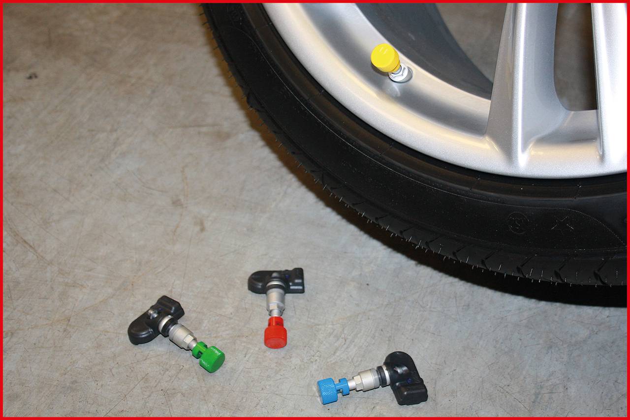 Ein Autoreifen mit einem gelben Ventil; daneben liegen drei farbige Ventile für den Reifendrucksensor auf dem Boden.