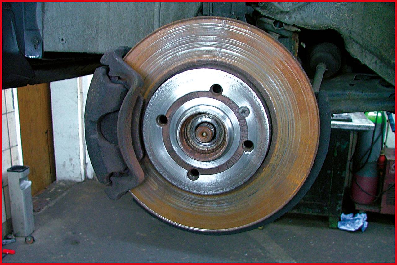Eine teilweise abgenutzte Autoscheibenbremse in einer Werkstattumgebung, montiert am Rad eines Fahrzeugs, mit sichtbarem Bremsbelag.