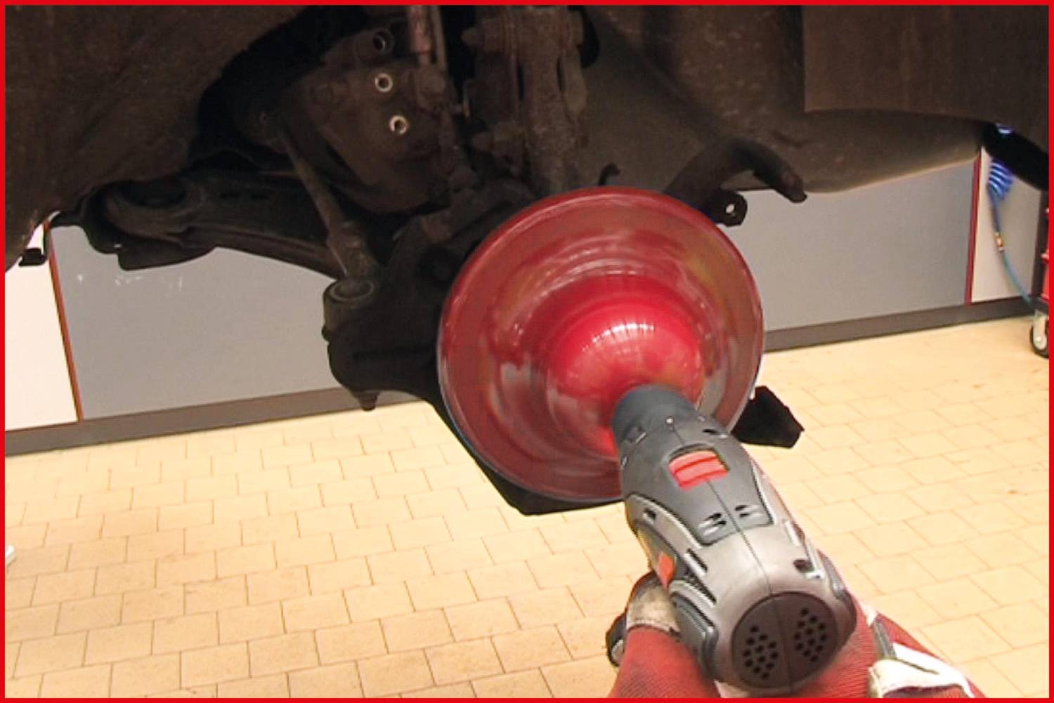 Nahaufnahme eines Autos, das in einer Werkstatt repariert wird. Ein Mechaniker poliert eine rotierende Bremsscheibe mit einem Spezialgerät.