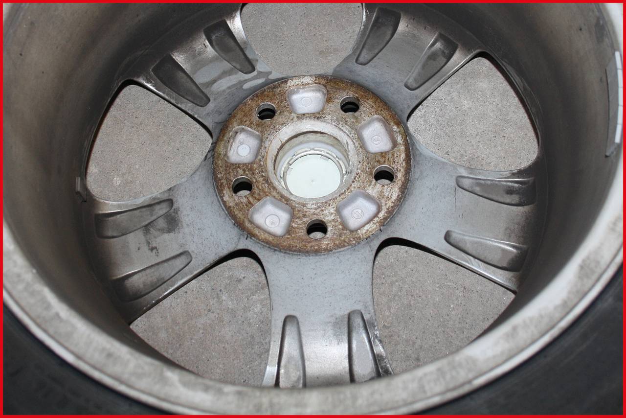 Die Rückseite einer Autofelge zeigt Rost um die Schraubenlöcher. Die Felge besteht aus Metall mit dunklen Markierungen auf der Innenseite.