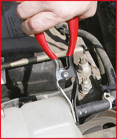 Eine Hand bedient eine rote Zange, um einen Metallobjekt an einem Autoteil zu lösen. Das Bild zeigt eine mechanische Reparaturarbeit.