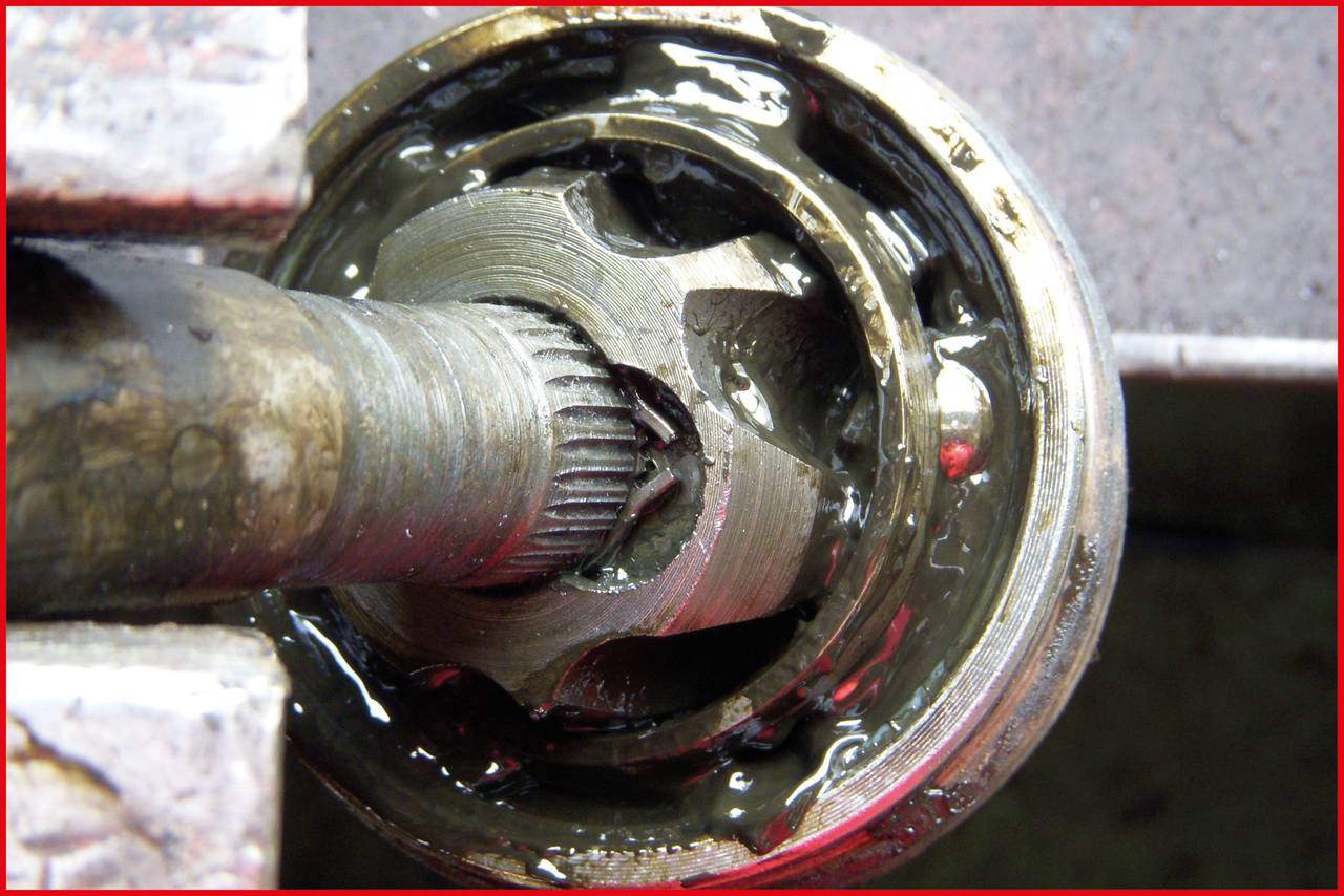 Nahaufnahme eines beschädigten Antriebsgelenks mit gebrochener Metallverzahnung, umgeben von Fett. Das Gelenk ist rostig und abgenutzt.