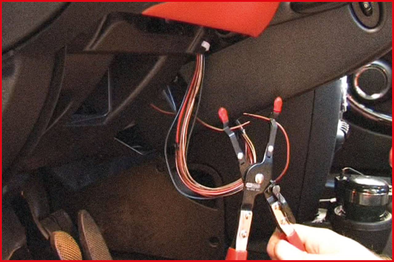 Eine Person hält ein Werkzeug, während sie an freiliegenden Kabeln unter einem Armaturenbrett arbeitet.