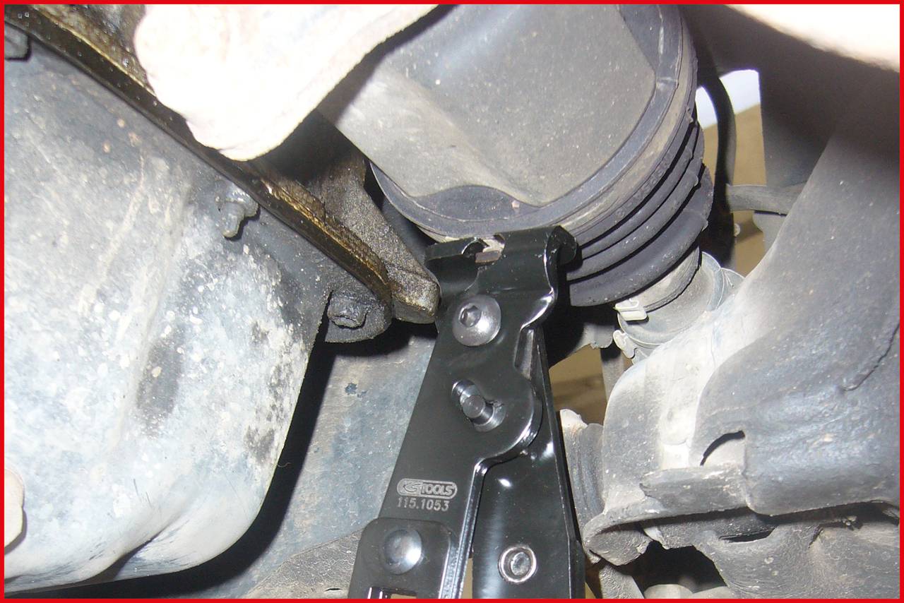 Ein Wagenheber stützt ein Fahrzeug, das an der Unterseite sichtbar ist. Der Wagenheber ist unter einer Metallachse positioniert.