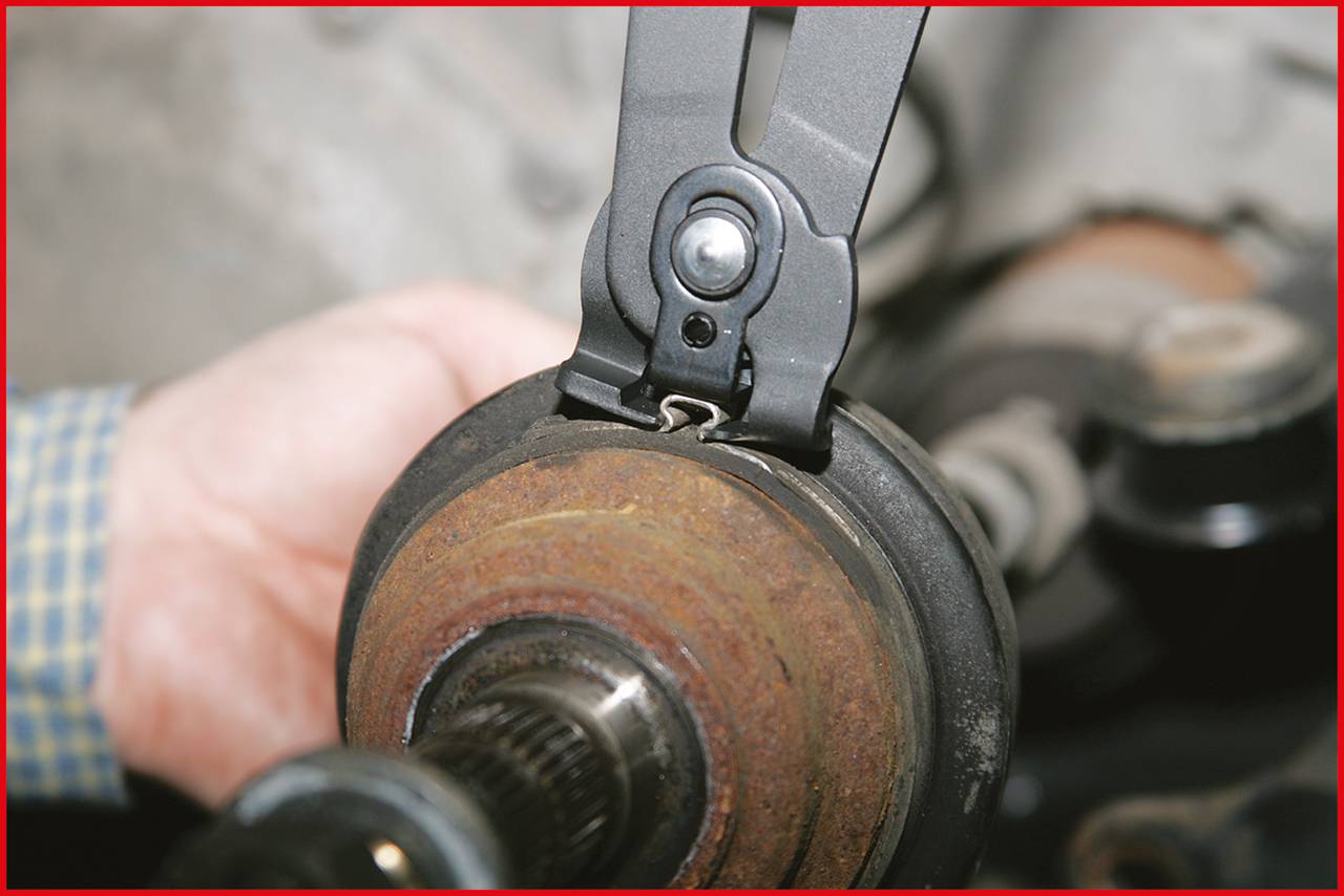 Eine Hand benutzt eine Zange, um eine selbstsichernde Mutter an einer rostigen Fahrzeugachse zu entfernen.