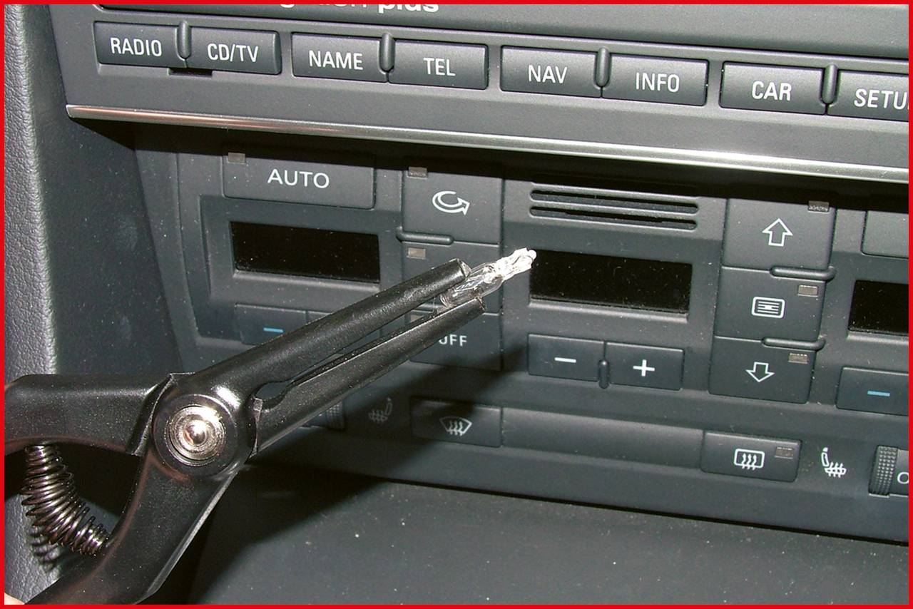 Eine Hand hält ein Spezialwerkzeug zum Entfernen eines Autoradios in einem Fahrzeug. Das Dashboard zeigt Knöpfe und Einstellungen.