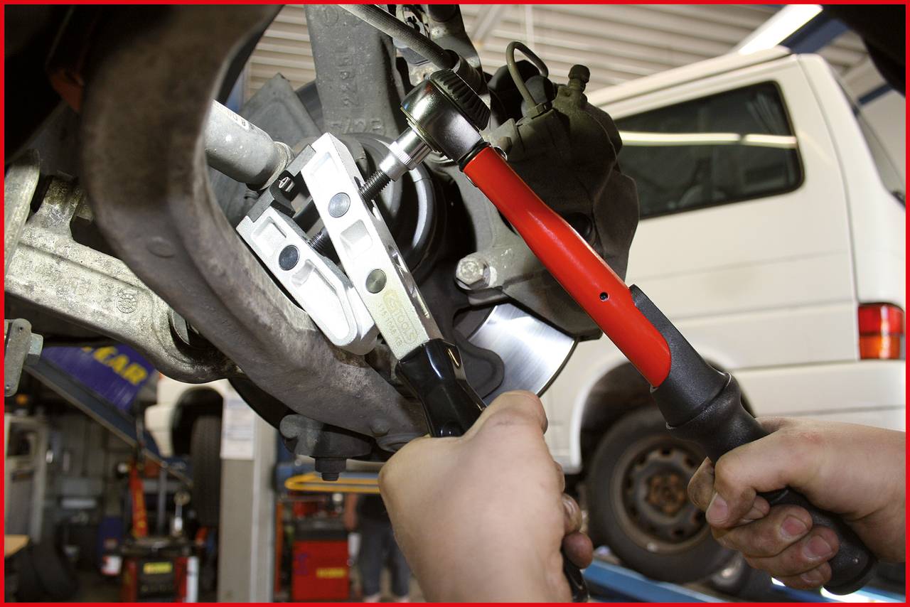 Mechaniker repariert Autoteil in Werkstatt, benutzt roten Schraubenschlüssel an Metallkomponente.