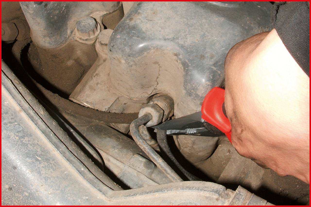 Hand hält Schraubenschlüssel und zieht Schraube an einer stark verschmutzten motorähnlichen Oberfläche fest.