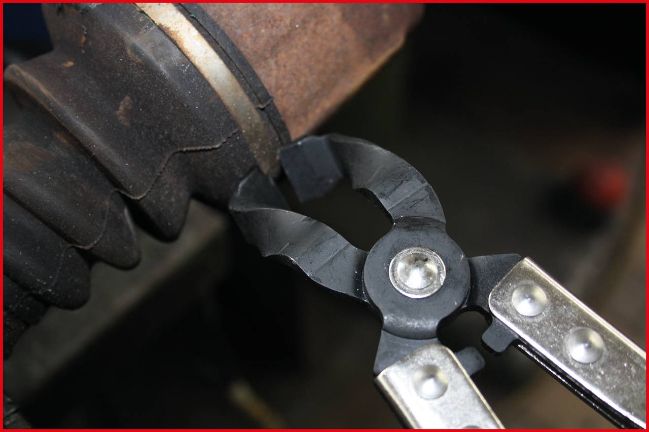 Eine Zange schneidet ein schwarzes Kabel, das über ein rostiges Metallrohr verläuft.