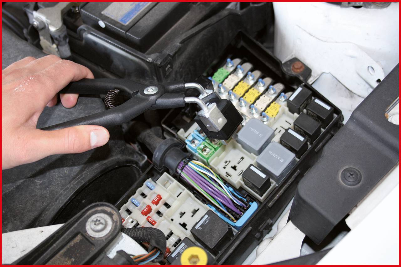 Eine Hand benutzt Zange, um eine Sicherung in einer Autosicherungskasten zu entfernen. Verschiedene farbige Sicherungen sichtbar.