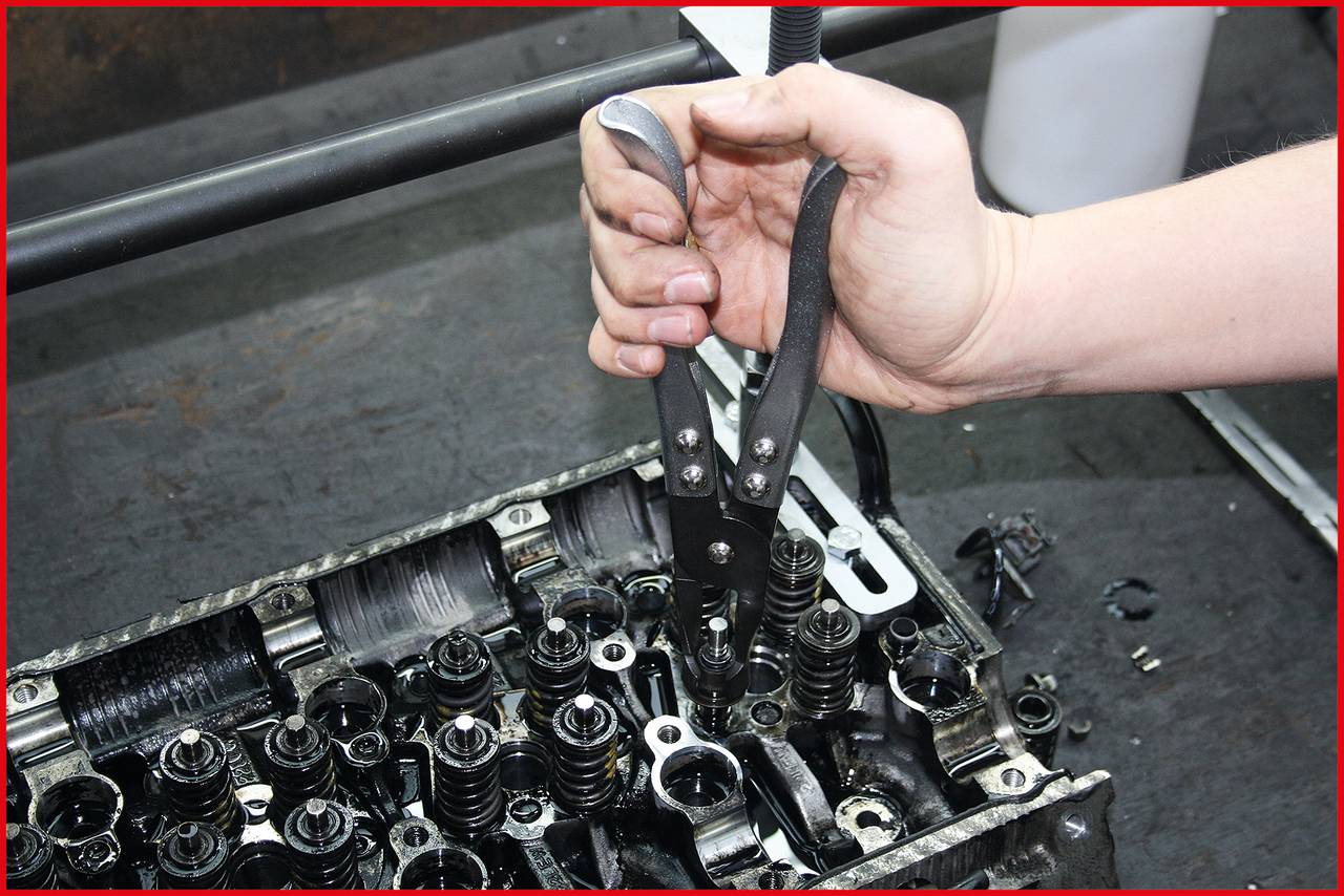 Eine Hand benutzt eine Zange, um an einem komplexen Motorteil zu arbeiten. Mehrere Ventile und Mechaniken sind sichtbar.