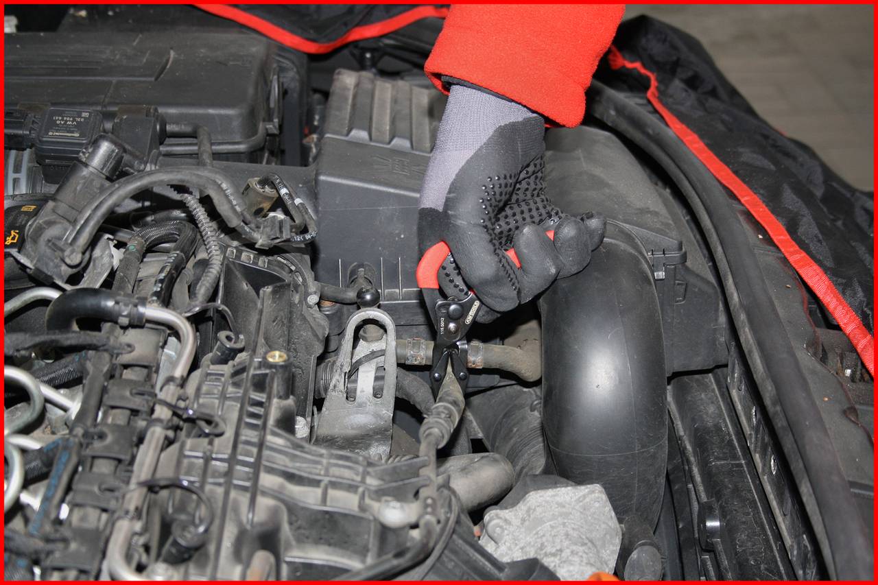 Eine Person in roten Handschuhen arbeitet am Motorraum eines Autos, prüft oder repariert Teile. Der Fokus liegt auf technischer Arbeit.