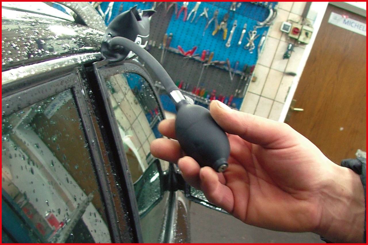 Eine Person benutzt ein Aufblaskissen und Werkzeug, um die Autotür zu öffnen. Hintergrund zeigt verschiedene Werkzeuge an der Wand.