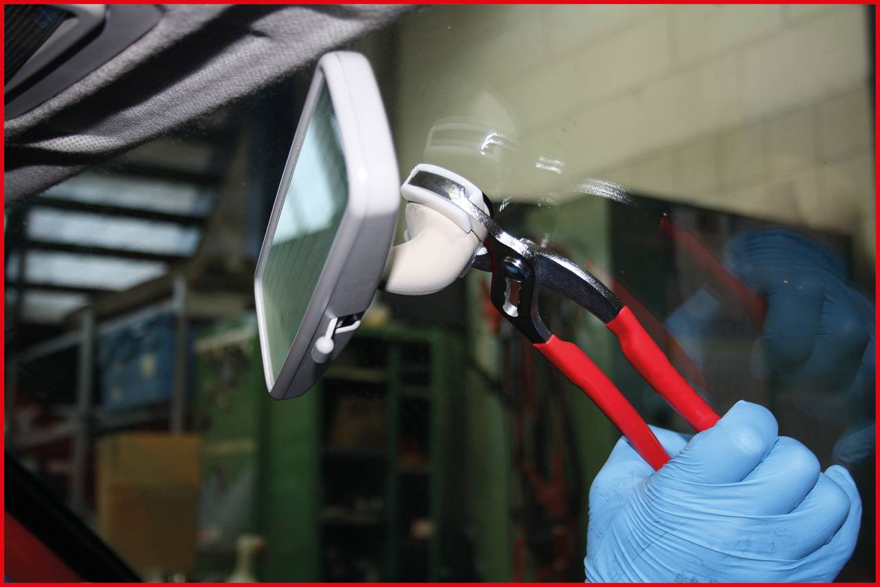 Eine Person mit blauen Handschuhen repariert einen Auto-Rückspiegel mit Zange im Inneren eines Autos.