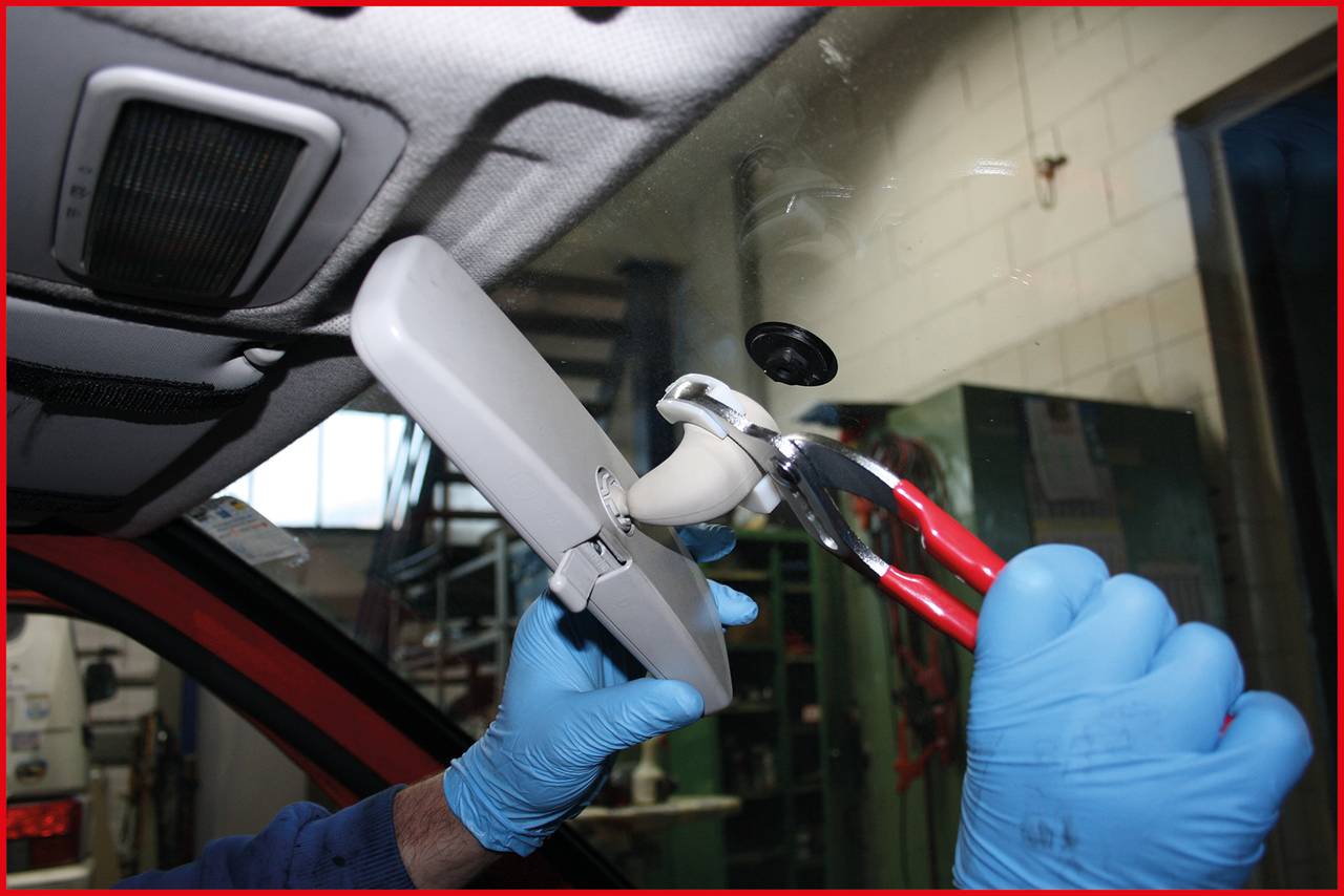 Eine Person mit blauen Handschuhen entfernt den Rückspiegel eines Autos mit einer Zange.