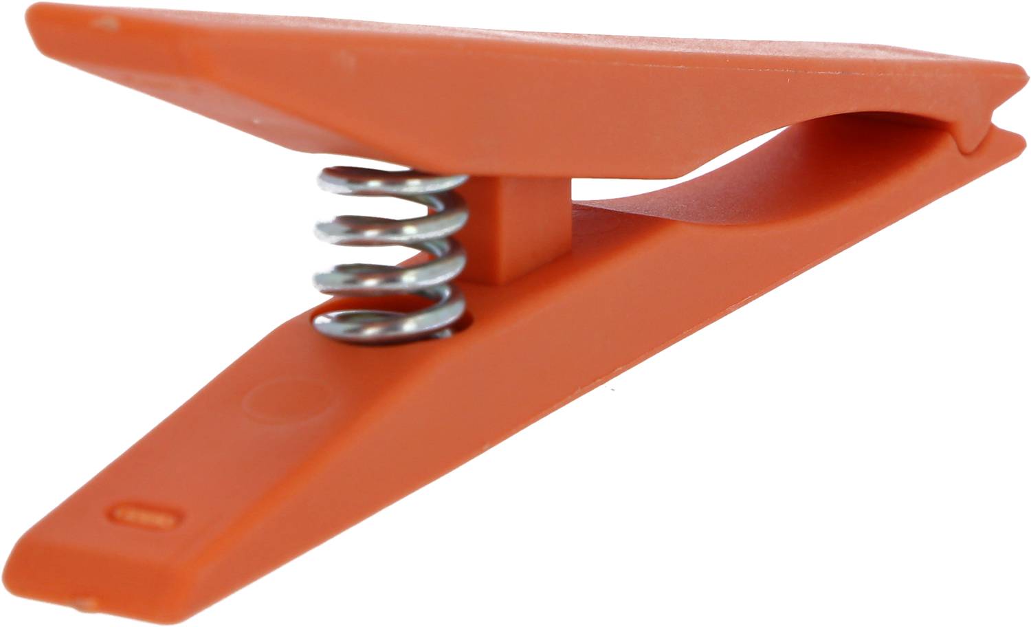 Ein orangefarbener Wäscheklammer aus Kunststoff mit Metallfeder, liegt schräg auf einer weißen Fläche.