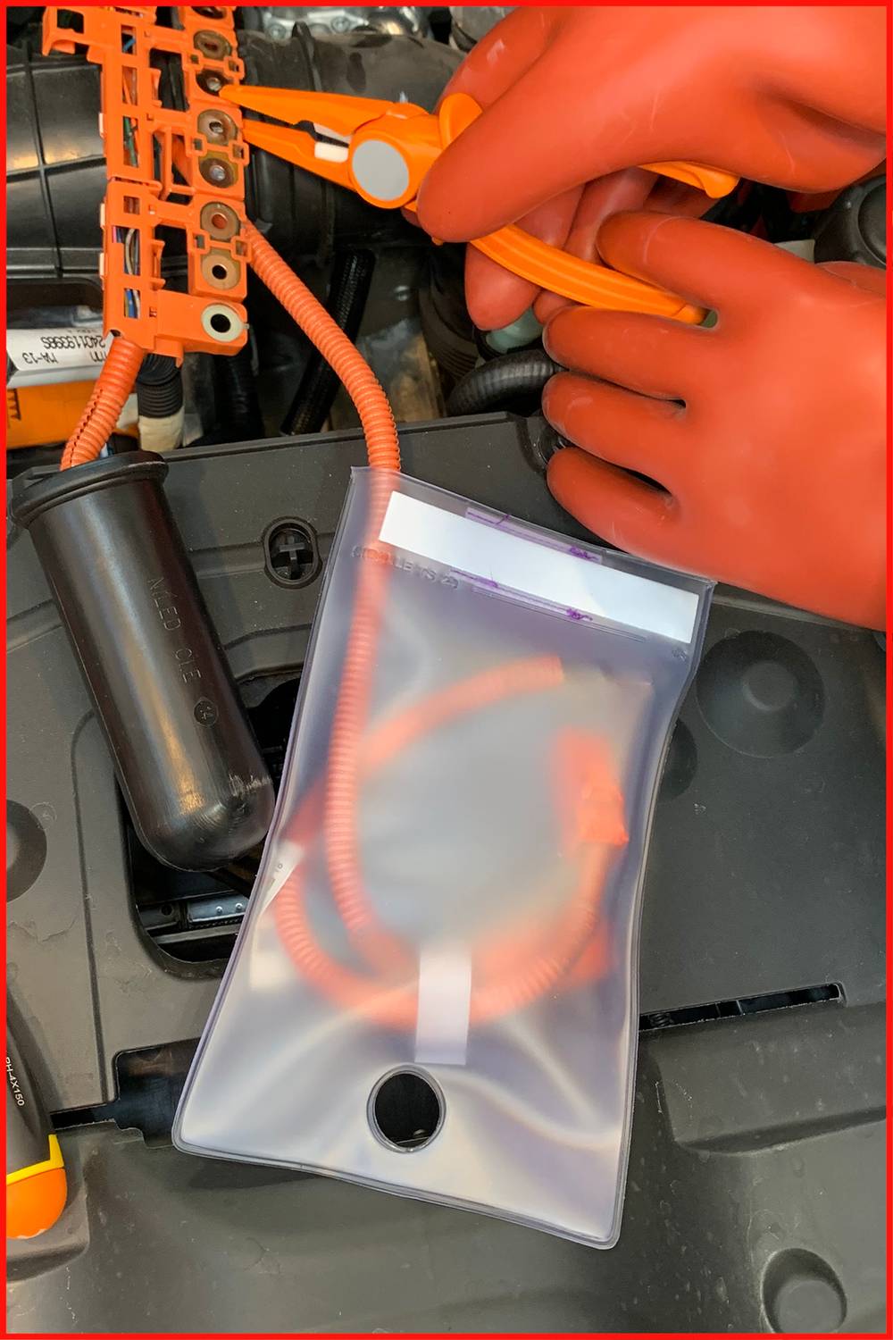 Mechanikerhände mit roten Handschuhen arbeiten in einem Auto an einem elektrischen Kabelstrang neben einem durchsichtigen Schutzbeutel.