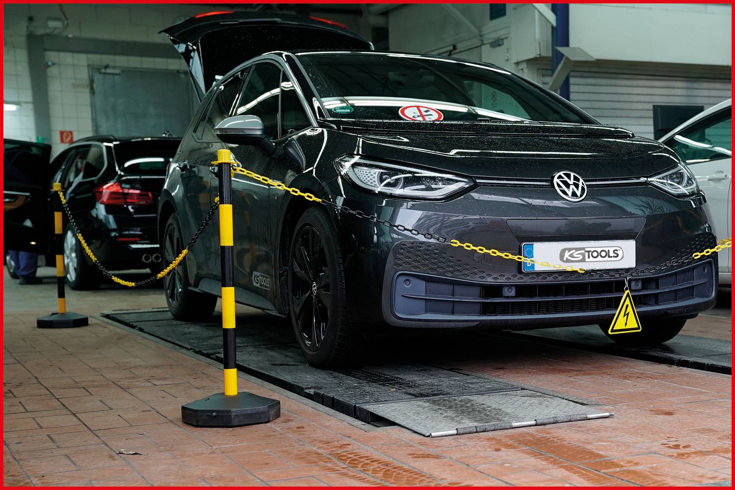 Ein schwarzer Volkswagen steht mit geöffneter Heckklappe in einer Autowerkstatt auf einem Hebebühne. Sicherheitsketten und Schilder sind sichtbar.