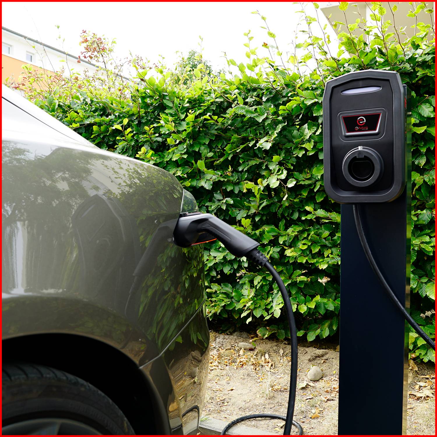 Ein Elektroauto wird an einer Ladesäule aufgeladen. Die Ladesäule hat ein Display und ist von grünen Büschen umgeben.